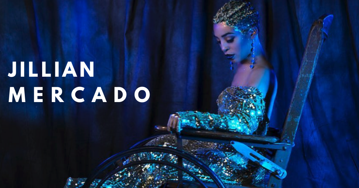 Jillian is in a glittering blue dress. She has olive toned skin and dyed white hair. She models in her wheelchair.