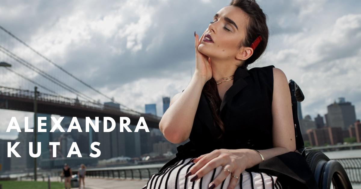 Alexandra models in a wheelchair. Her dark dress and hair contrast with the cloudy grey sky behind her.