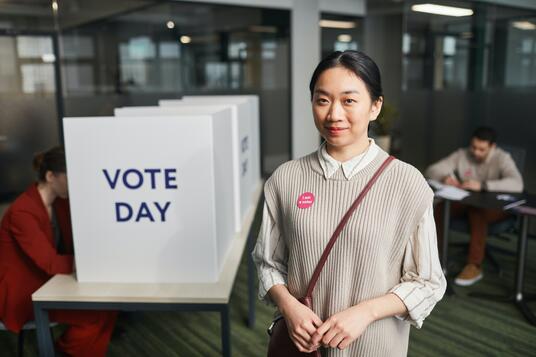 Are you enrolled to vote? An Asian Australian woman stands in front of a ballot box.